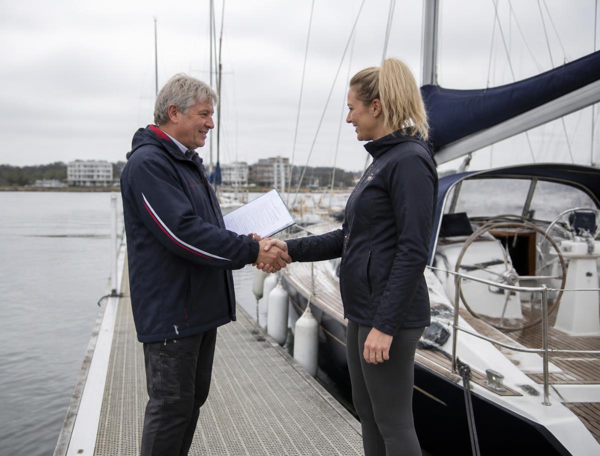 A buyer and seller shaking hands on a pontoon beside a yacht, holding sale documents
